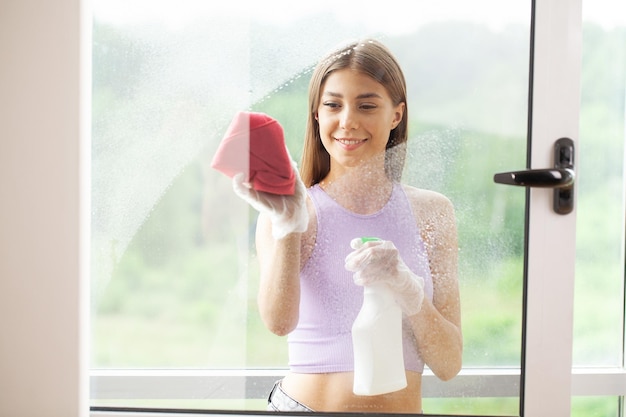 Hermosa joven está usando un trapo mientras limpia ventanas