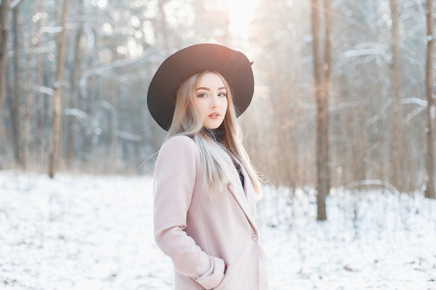 Hermosa joven con estilo en un abrigo y sombrero negro de moda en el día soleado de invierno