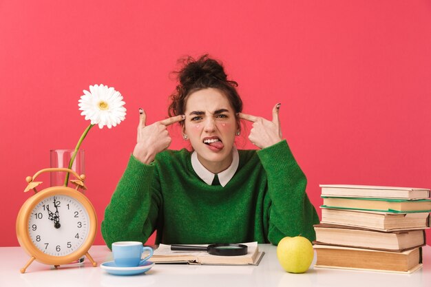 Hermosa joven estudiante aburrida sentada en la mesa aislada, estudiando con libros