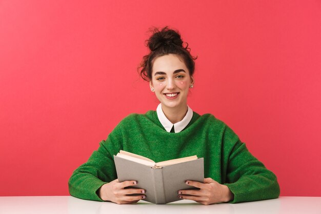 Hermosa joven estudiante nerd sentada en la mesa aislada, estudiando con libros,