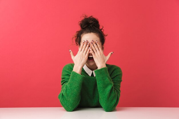 Foto hermosa joven estudiante sentada en la mesa aislada, cubrir la cara