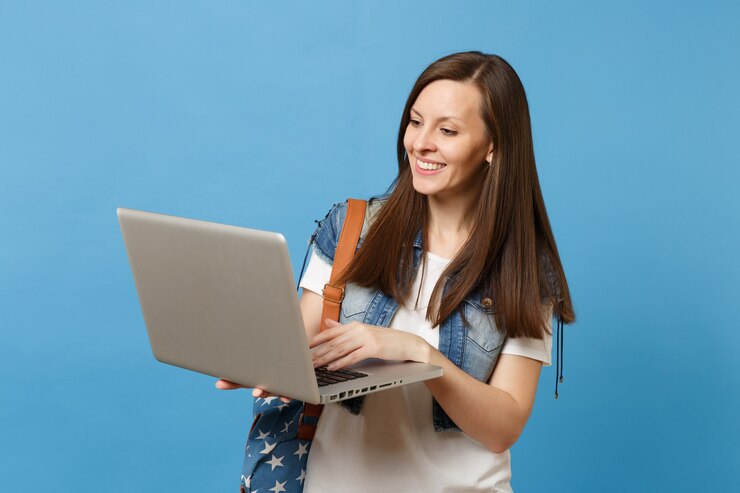Foto hermosa joven estudiante sonriente en ropa de mezclilla con mochila sosteniendo y usando el trabajo en la computadora portátil pc aislada sobre fondo azul. educación en la universidad. copie el espacio para publicidad.