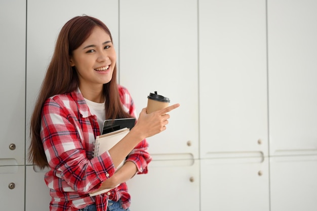 Hermosa joven estudiante universitaria asiática con sus cosas parada frente al casillero