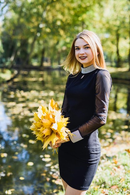 Hermosa joven estudiante vestida de negro con un ramo de hojas en el parque de otoño.