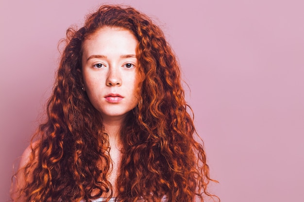 Hermosa joven con estudio de pelo largo rojo fuego sobre un fondo rosa Sin maquillaje ni retoques