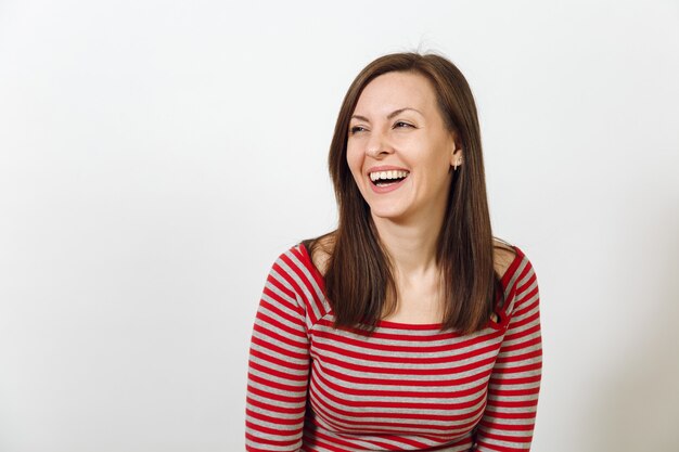 La hermosa joven europea feliz de cabello castaño con una piel limpia y saludable y una sonrisa encantadora, vestida con ropa casual de color rojo y gris, riendo y disfrutando sobre un fondo blanco. Concepto de emociones.