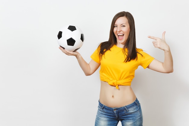 Hermosa joven europea fuerte delgada sexy mujer, aficionado al fútbol o jugador en uniforme amarillo con balón de fútbol aislado sobre fondo blanco. Deporte, fútbol, salud, concepto de estilo de vida saludable.