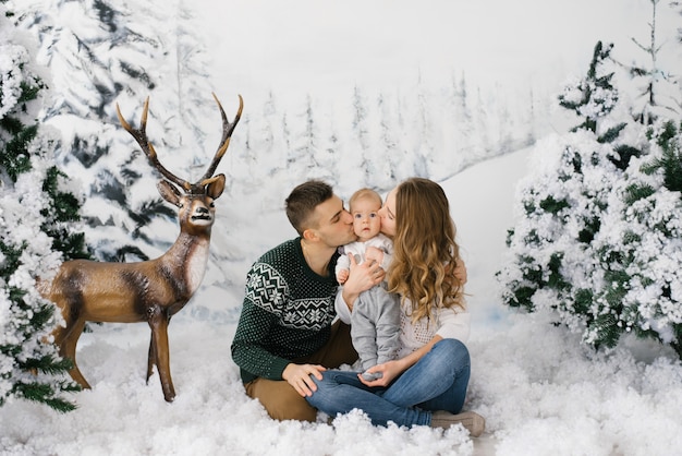 Hermosa joven familia besa a su pequeño hijo en la zona de fotos de invierno