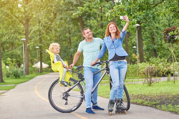 Hermosa joven familia feliz disfrutando de andar en bicicleta y patinar en el campo.