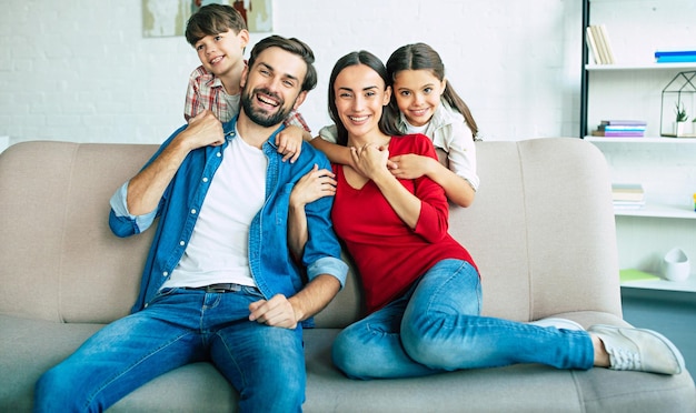 Hermosa joven familia feliz relajándose juntos en casa sonriendo y abrazándose