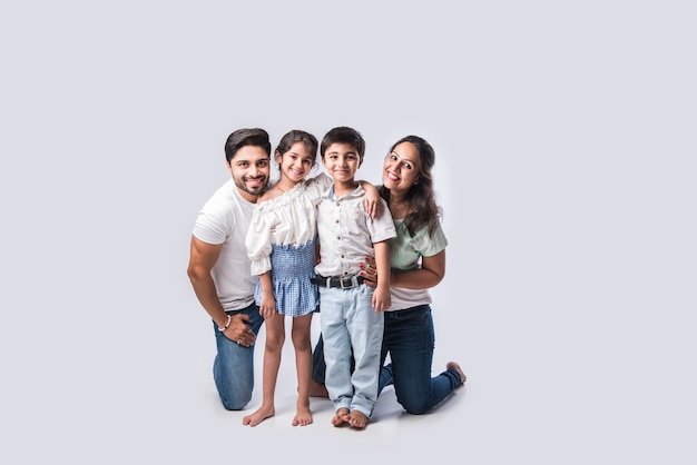 Hermosa joven familia india de cuatro abrazos, mirando a puerta cerrada y sonriendo mientras está de pie contra el fondo blanco.