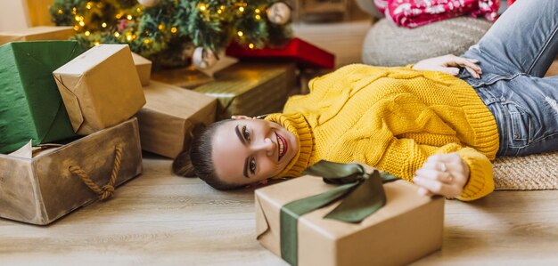 Hermosa joven feliz alegre con regalos de Navidad en el fondo de un árbol de año nuevo en casa