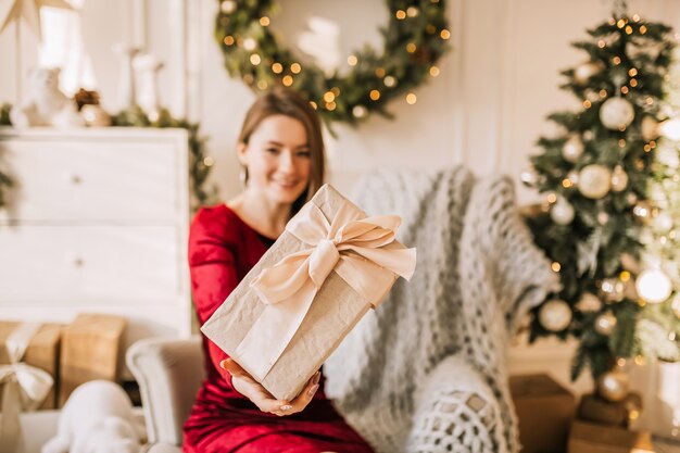 Hermosa joven feliz alegre con regalos de Navidad en el sofá en el fondo de un árbol de año nuevo en casa