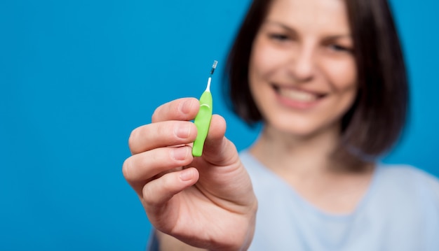 Hermosa joven feliz con cepillo interdental sobre fondo azul.