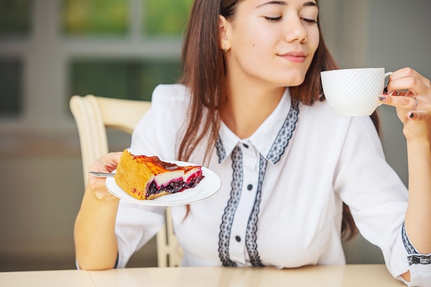 Hermosa joven feliz desayunando café y tarta de queso sentado en la mesa