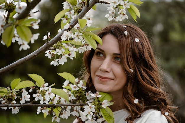Hermosa joven feliz disfrutando de las flores y oliendo el árbol de flores en el jardín de primavera