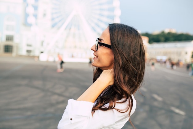 Hermosa joven feliz con gafas pasándola bien en la plaza de la ciudad mientras camina al aire libre