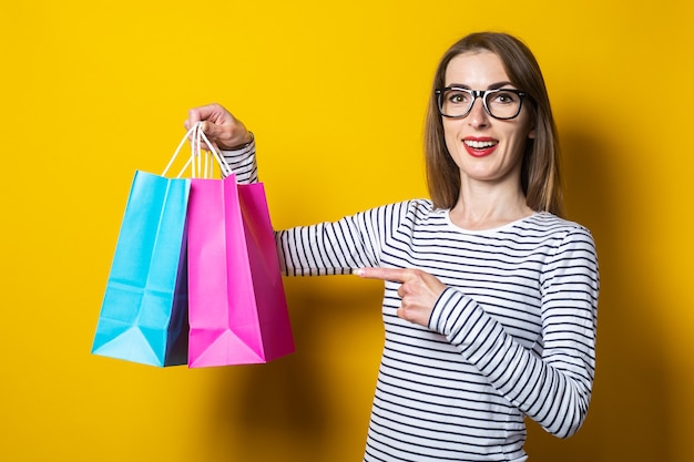 Hermosa joven feliz señala con el dedo bolsas de la compra sobre un fondo amarillo