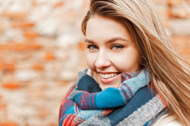 Hermosa joven feliz sonriendo con una sonrisa perfecta y dientes blancos cerca de la pared de ladrillo y mirando a la cámara