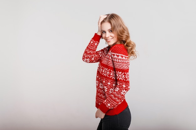 Hermosa joven feliz en un suéter rojo vintage de moda sobre un fondo gris en el estudio