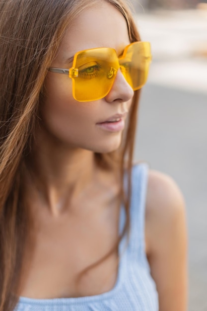 Hermosa joven glamorosa en ropa de verano de moda brillante con gafas amarillas con estilo en la calle