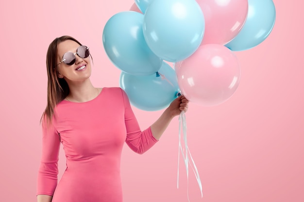 Hermosa joven con globos azules y rosas en pared rosa.