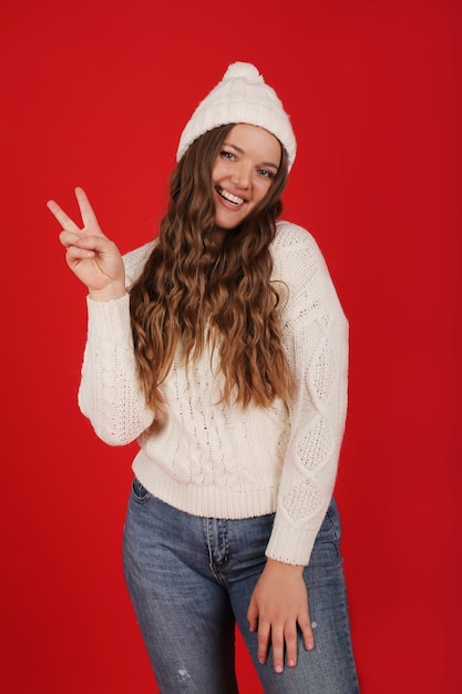 Una hermosa joven con un gorro de invierno y un suéter de punto en jeans sobre un fondo rojo.