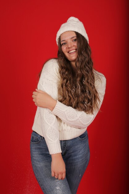 Una hermosa joven con un gorro de invierno y un suéter de punto en jeans sobre un fondo rojo.