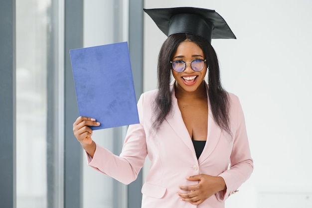 Hermosa joven graduado afroamericano en traje académico tiene diploma