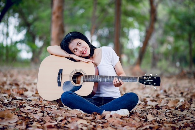 Hermosa joven guitarrista tocando la guitarra felizmente en el jardín, bosque natural, concepto de música