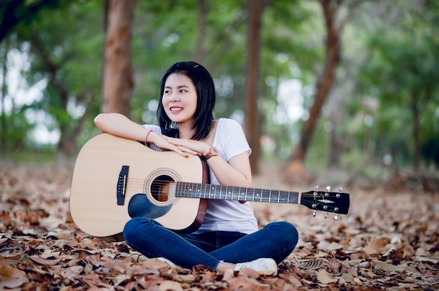 Hermosa joven guitarrista tocando la guitarra felizmente en el jardín, bosque natural, concepto de música