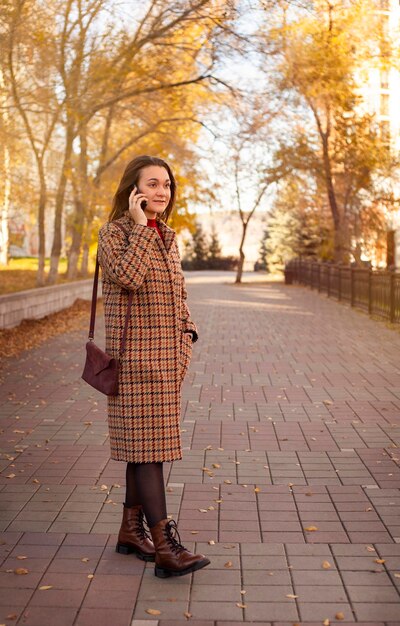 Hermosa joven hablando por teléfono en el parque de otoño