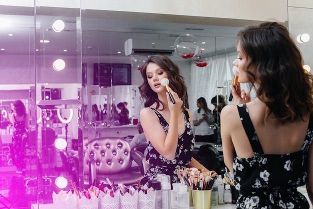 Una hermosa joven hace un hermoso maquillaje de noche frente al espejo. Moda y belleza.