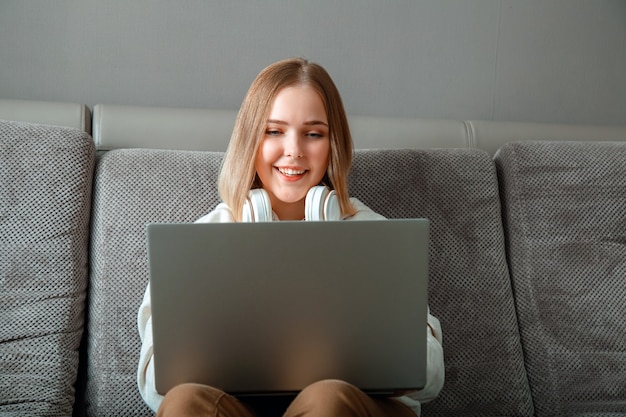 Hermosa joven hacer estudio en línea de trabajo remoto desde casa a través de la computadora portátil. El adolescente tiene un espacio de trabajo conveniente con computadora portátil. Adolescente en la oficina en casa acogedora en el trabajo remoto del freelancer del sofá usando la computadora portátil.