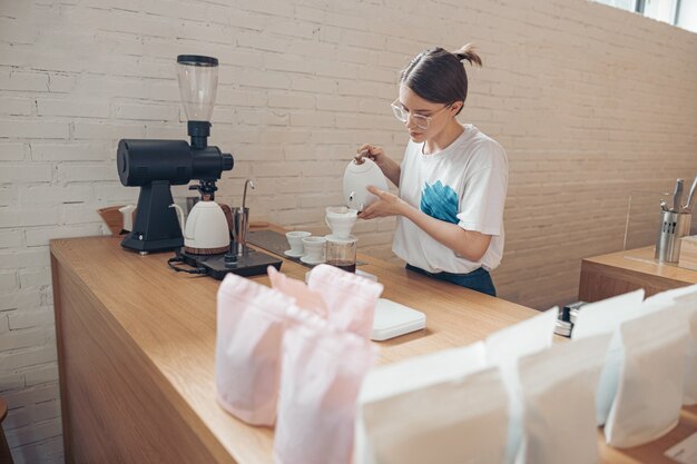 Hermosa joven haciendo café de filtro en la cafetería.