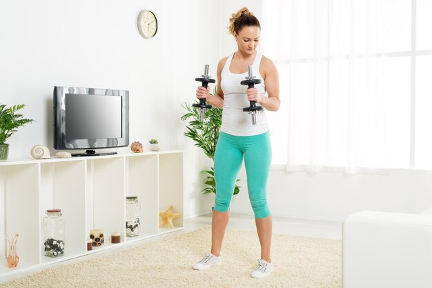 Hermosa joven haciendo ejercicio para fortalecer tríceps con pesas en casa.