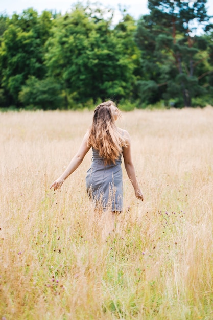 Hermosa joven con hermoso cabello largo con un vestido gris camina por el campo