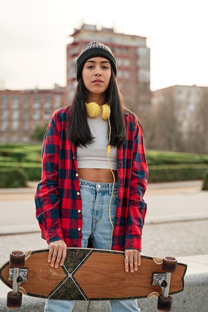 Hermosa joven hipster posando con monopatín Mujer latina hispana con ropa informal