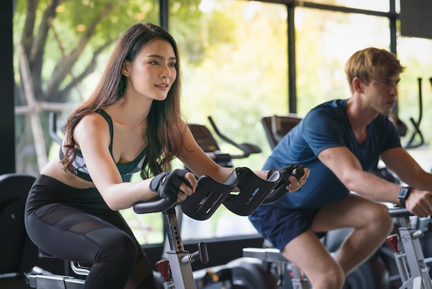 Hermosa joven y hombre haciendo ejercicio en bicicleta estacionaria en el gimnasio gimnasio club deportivo