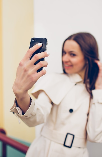 Hermosa joven en un impermeable ligero toma un selfie en su teléfono