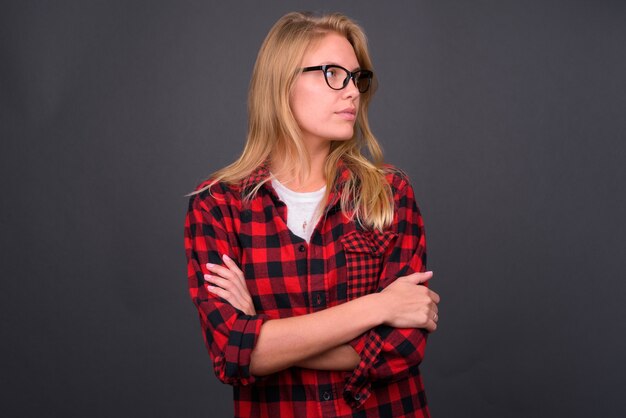 Hermosa joven inconformista con cabello rubio con anteojos contra la pared gris