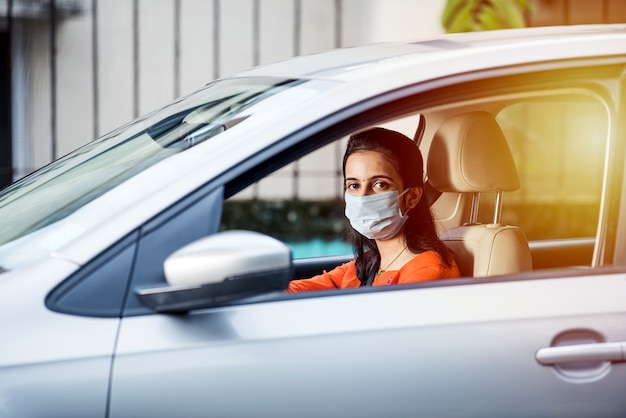 Hermosa joven india con una máscara sentada en un automóvil, máscara protectora contra el coronavirus, conductor en una calle de la ciudad durante la pandemia del covid-19