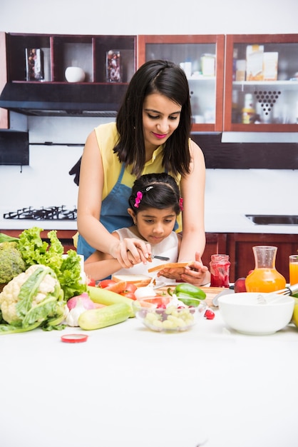 Hermosa joven india o asiática, madre e hija en la cocina, con mesa llena de frutas y verduras