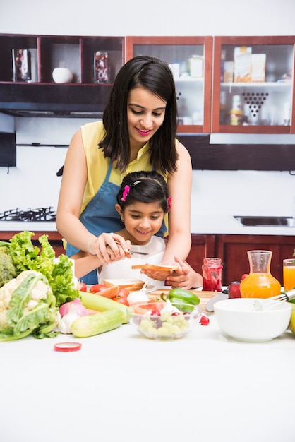 Hermosa joven india o asiática, madre e hija en la cocina, con mesa llena de frutas y verduras