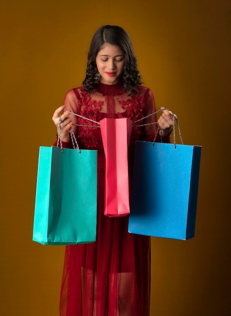 Hermosa joven india sosteniendo y posando con bolsas de compras en un fondo marrón