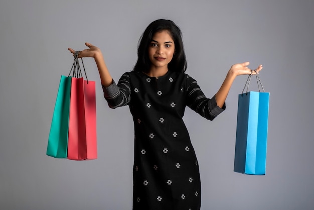 Hermosa joven india sosteniendo y posando con bolsas de compras en gris