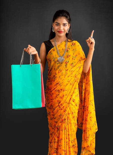 Hermosa joven india sosteniendo y posando con bolsas de compras sobre un fondo gris