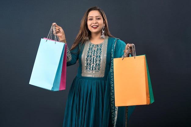 Hermosa joven india sosteniendo y posando con bolsas de compras sobre un fondo gris