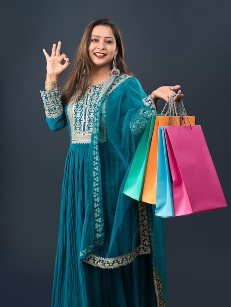 Hermosa joven india sosteniendo y posando con bolsas de compras sobre un fondo gris