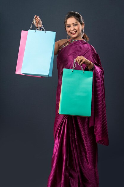 Hermosa joven india sosteniendo y posando con bolsas de compras sobre un fondo gris